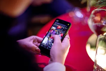 A cheerful woman in traditional clothing using her smartphone during a festive moment, showing how easily the JLWAFA app fits into everyday life.