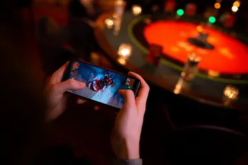 A player using their smartphone during a festive local event, representing JLWAFA’s fully mobile-friendly casino.